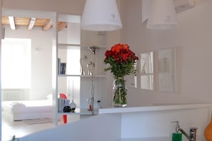 A modern bathroom with a white vanity, a vase of red flowers, and a green soap dispenser.