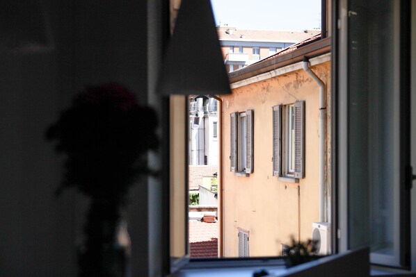 A view through a window with a flower in the foreground, a building with shutters, and a clear sky.