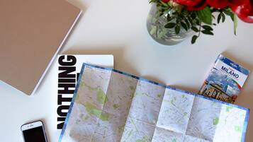 A map, a notebook, a smartphone, and a book titled "MILANO" on a table.