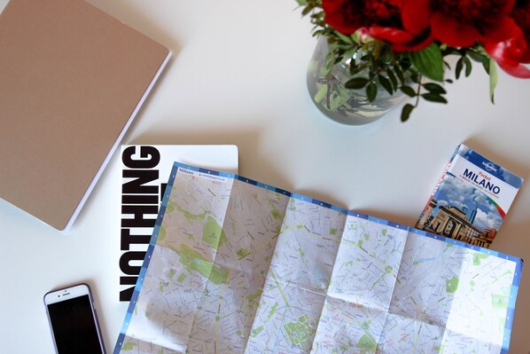 A map, a notebook, a smartphone, and a book titled "MILANO" on a table.