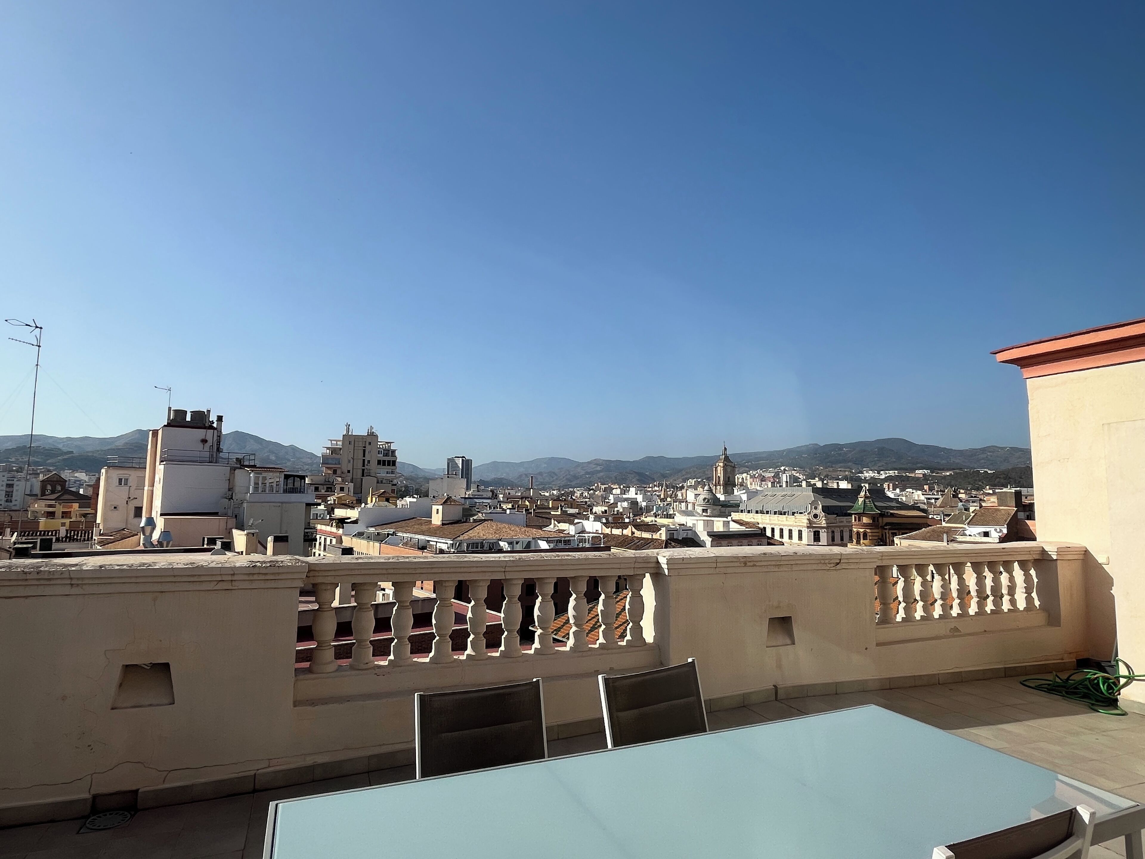 Una terrazza sul tetto con un tavolo e sedie, vista su un paesaggio urbano con edifici e montagne all'orizzonte.