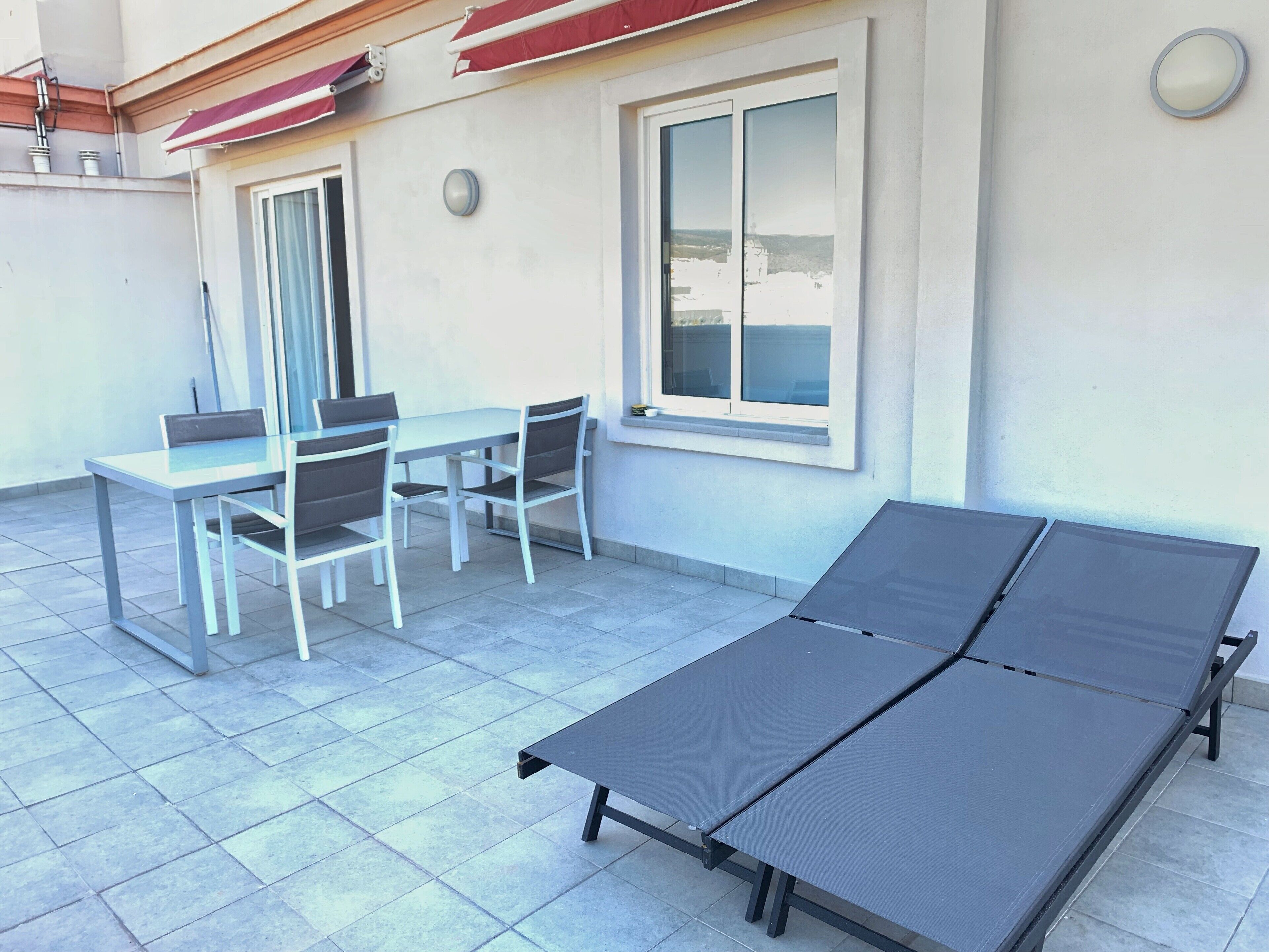 A patio with a table and chairs, a sun lounger, and a window with a view.