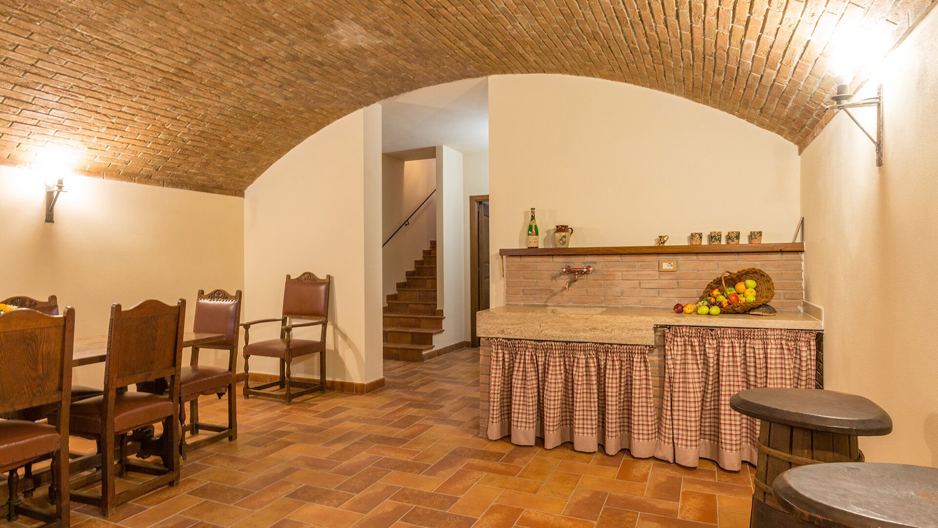 A kitchen with a brick ceiling, a dining area with wooden chairs, and a staircase leading to another room.