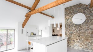 A modern kitchen with a large island, stone wall, and wooden beams. - Owl Barn Great Brecon Beacons views A stylish modern barn conversion for 5. (Llandovery)