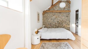 A bedroom with a stone wall, wooden beams, a bed, a bedside table, and a white lamp. - Owl Barn Great Brecon Beacons views A stylish modern barn conversion for 5. (Llandovery)