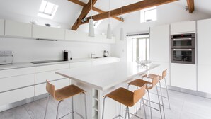 A modern kitchen with white cabinetry, a large island with bar stools, pendant lights, and a built-in oven. - Owl Barn Great Brecon Beacons views A stylish modern barn conversion for 5. (Llandovery)