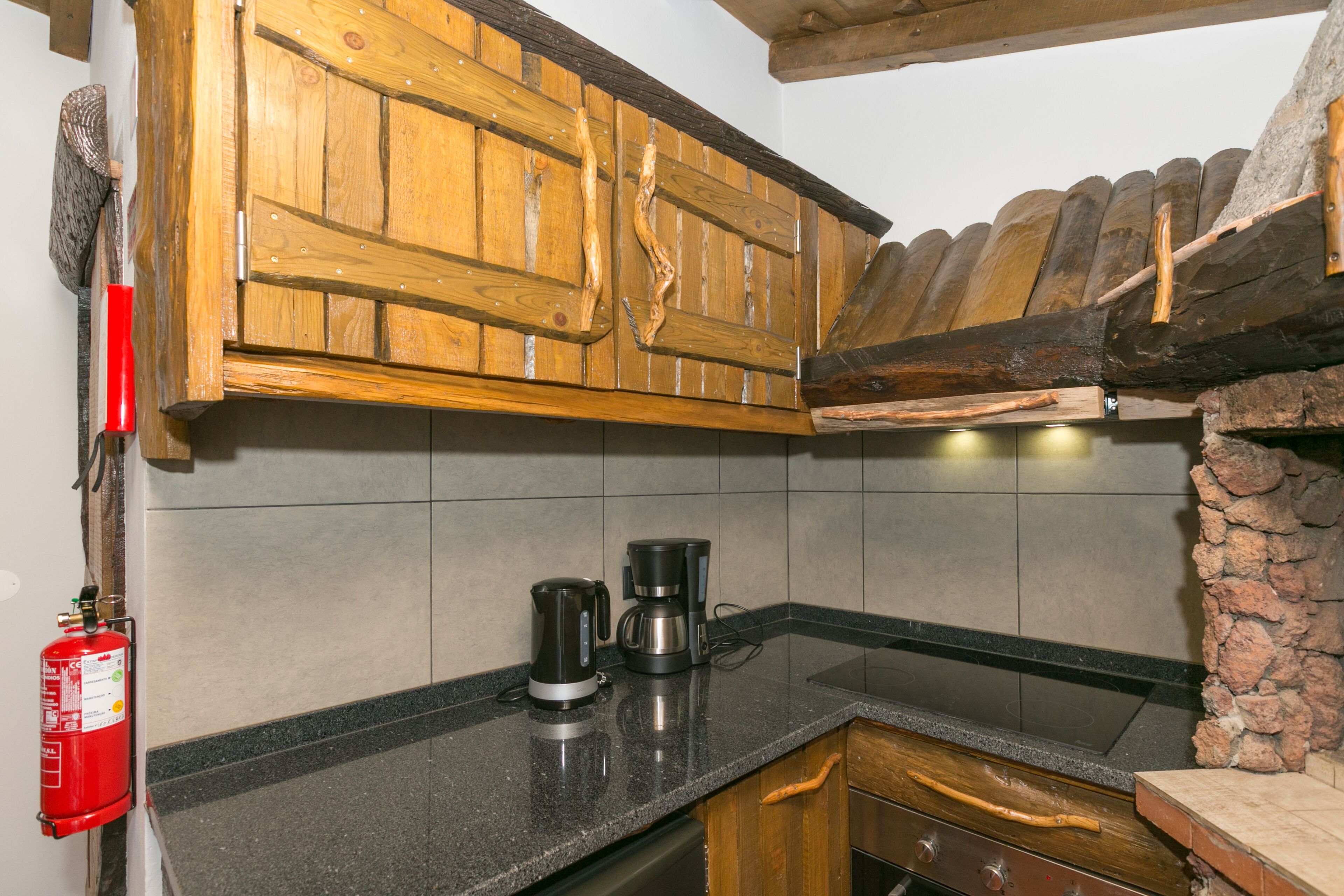 A kitchen with wooden cabinets, a granite countertop, a coffee maker, and a stone accent wall.