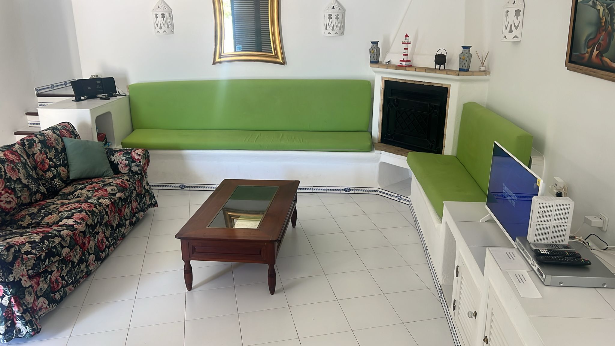 A living room with a green sofa, a floral couch, a wooden coffee table, a fireplace, and a television.