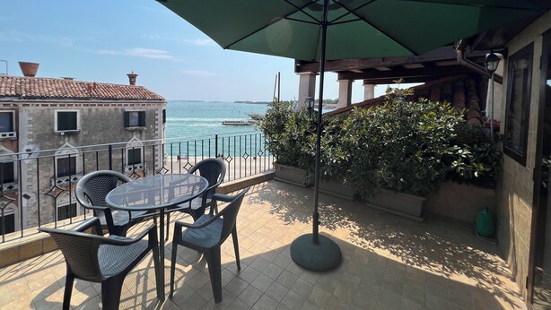 Una terraza con mesa y sillas, un parasol verde y vistas al mar.