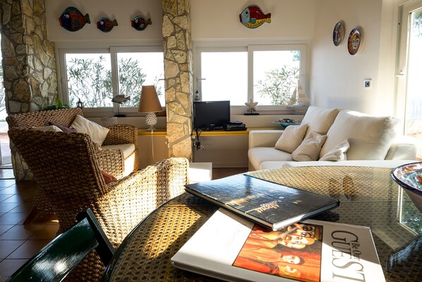 A cozy living room with wicker furniture, a laptop, and a book titled "Be Our Guest."