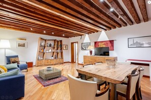 A spacious living area with a wooden ceiling, a dining table, and a blue sofa.