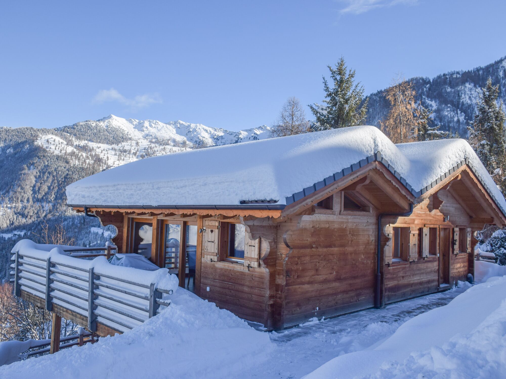 Une cabane en bois, dont le toit est recouvert de neige, entourée de neige et de montagnes.