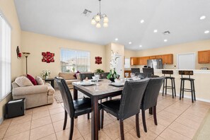 A spacious living area with a dining table, chairs, a sofa, and a kitchen area with cabinets and appliances.