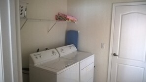 A laundry room with a front-loading washer and dryer, a shelf with folded clothes, and a door to the right.