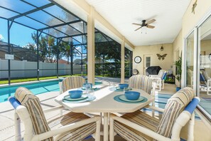 A covered outdoor dining area with a pool, chairs, and a table set for two.