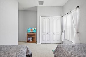 A bedroom with two beds, a TV on a wooden stand, and a white door.