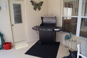 A patio with a black grill, a butterfly decoration, a red bucket, and a black mat.
