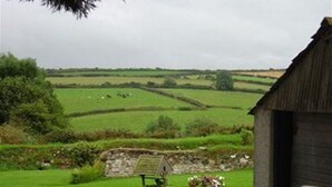 A rural landscape with a stone wall, a wooden structure, and a flower bed. - Country cottage near Boscastle, Situated amid the beautiful Cornish Countryside (Treneglos)