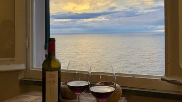 A bottle of wine and two glasses on a wooden table by a window overlooking the sea.
