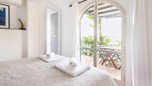 Ein Schlafzimmer mit einem Bett, zwei Handtüchern, einem gerahmten Bild und Blick auf einen Balkon mit Gartenmöbeln.