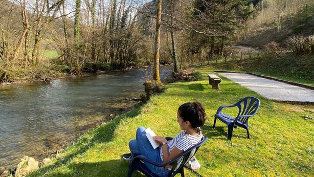 A person sitting on a chair by a river, reading a book. - Very beautiful 3* Cottage on the riverside, quiet in a green setting (Nans-Sous-Sainte-Anne)