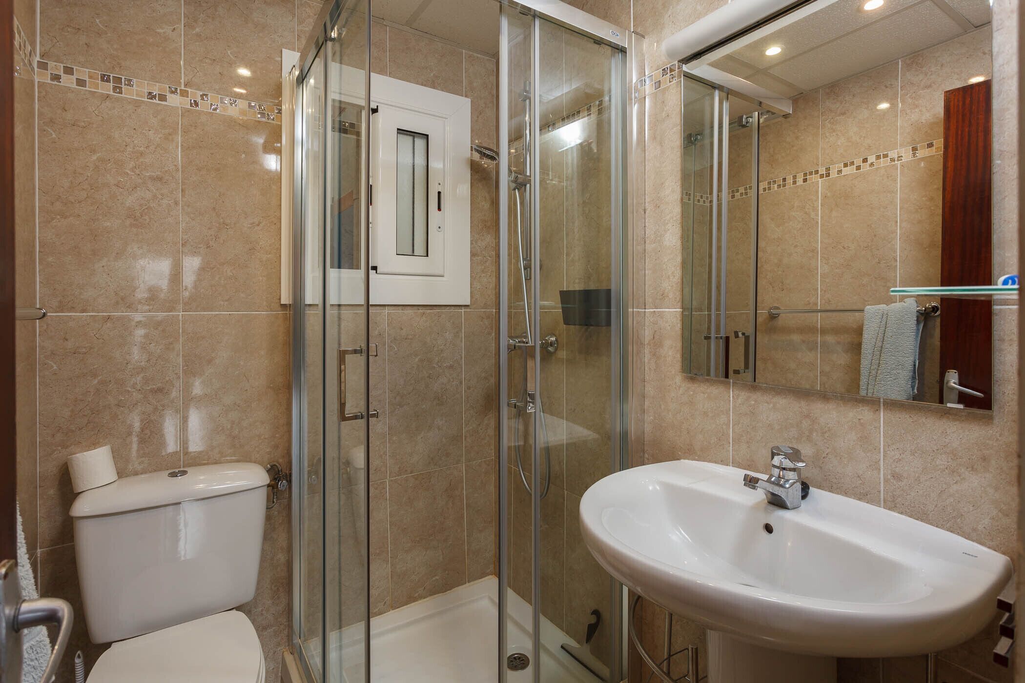 A bathroom with a glass-enclosed shower, a toilet, and a sink with a mirror above it.