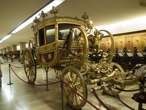 A golden carriage with intricate designs, surrounded by other exhibits in a museum setting.