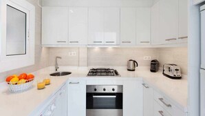 A modern kitchen with white cabinets, a gas stove, an oven, a kettle, and a toaster. - Sitges Bellavista Spectacular Sea Views (Sitges)