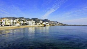 A coastal town with buildings along the beach, calm water, and mountains in the background. - Sitges Bellavista Spectacular Sea Views (Sitges)