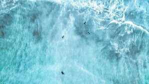 An aerial view of a beach with clear turquoise water and three surfers. - Sitges Bellavista Spectacular Sea Views (Sitges)