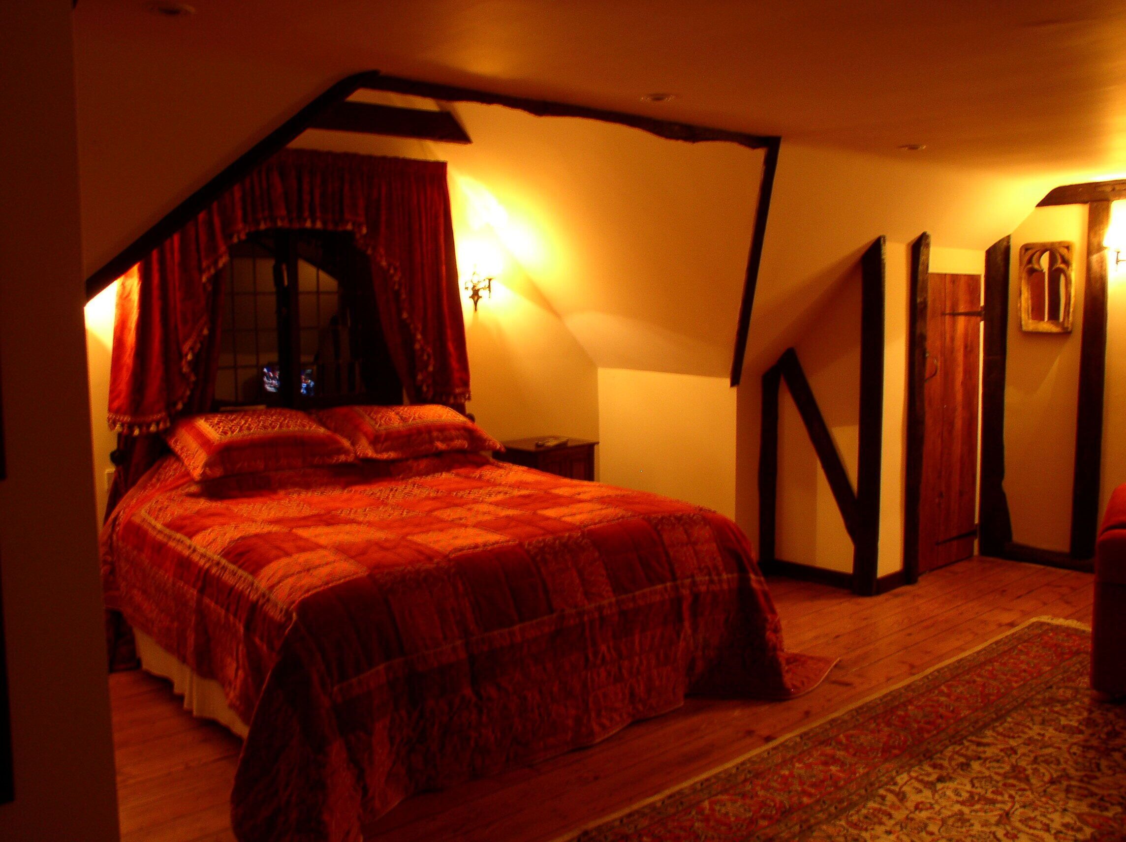 A bedroom with a large bed, a window with curtains, a wooden floor, and a nightstand.