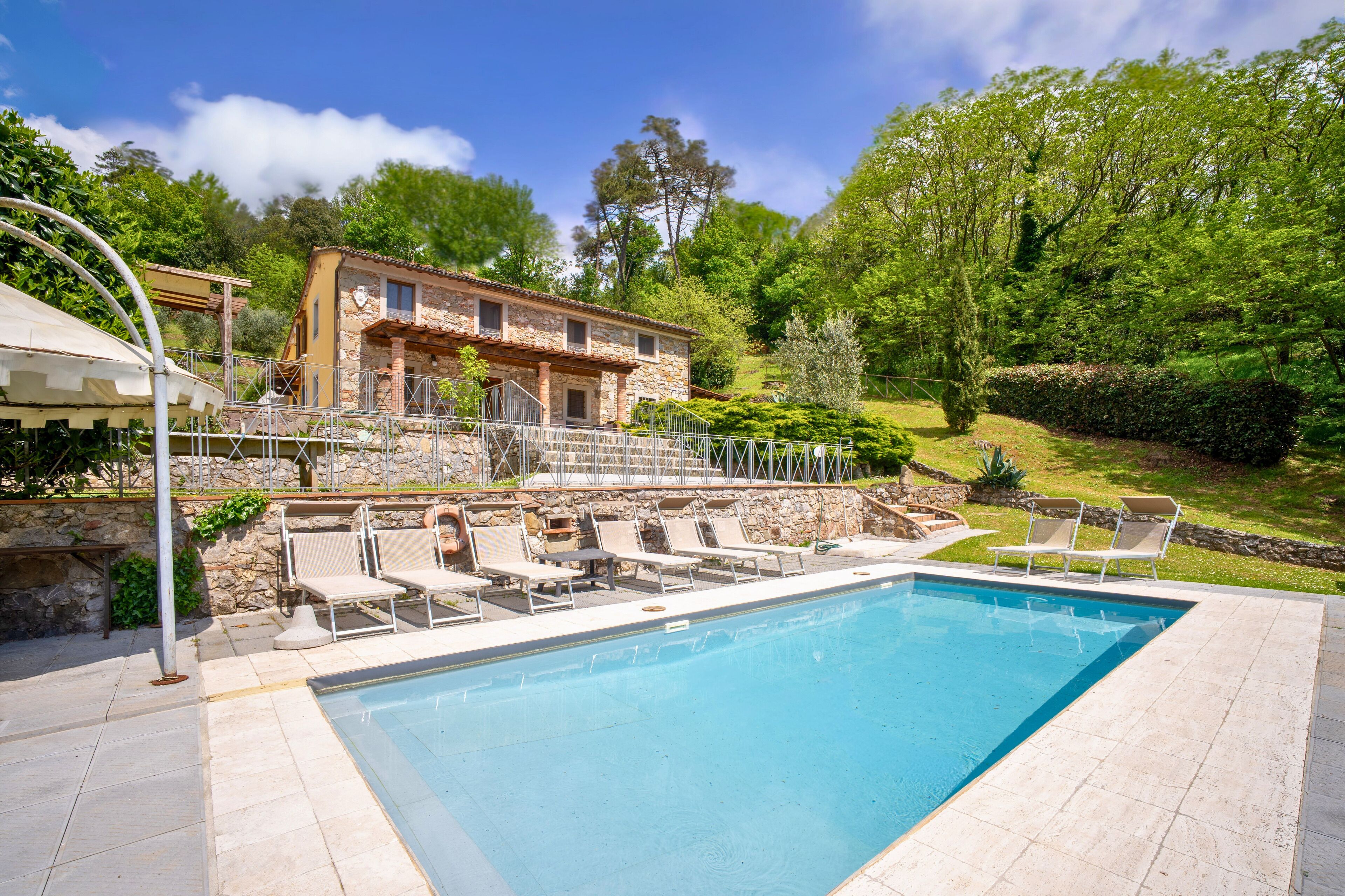A swimming pool with lounge chairs, a stone building, and lush greenery in the background.