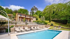 Ein Schwimmbecken mit Liegestühlen, ein Steinhaus und üppiges Grün im Hintergrund.