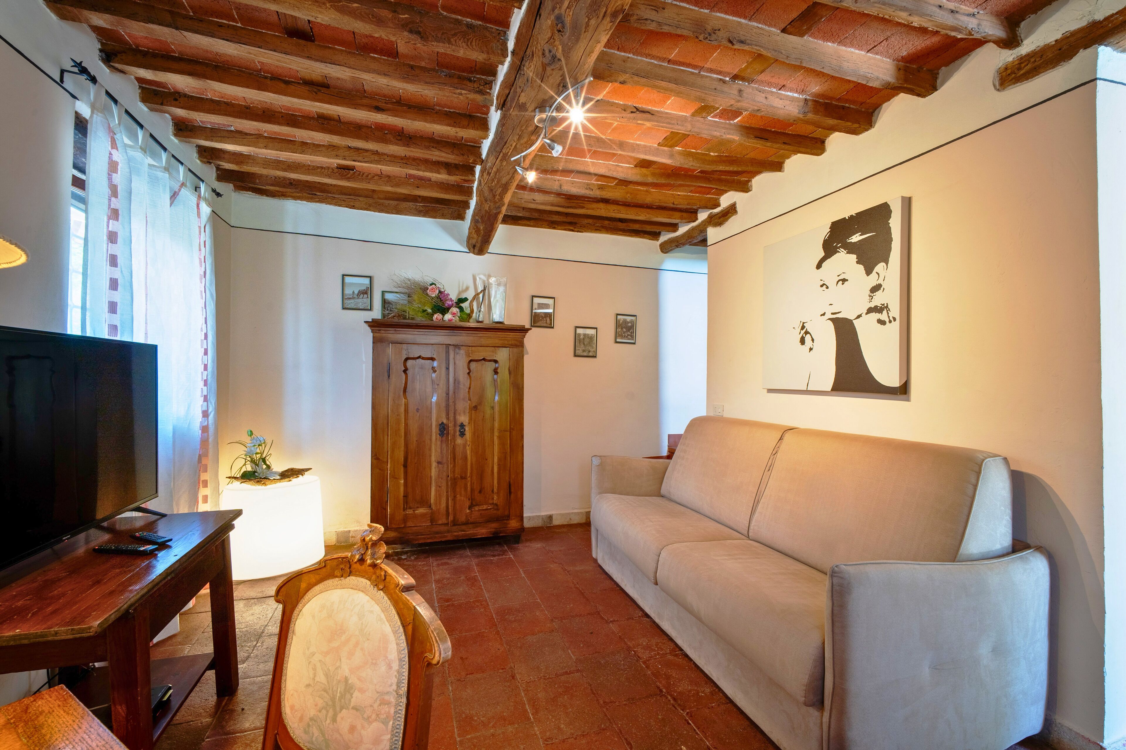A living room with a wooden ceiling, a sofa, a television, and a cabinet with decorative items.