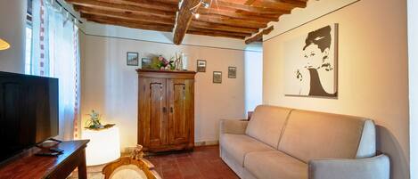 A living room with a wooden ceiling, a sofa, a television, and a cabinet with decorative items.