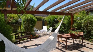 Un patio couvert avec un hamac, une table en bois, des chaises et un sol en pierre.