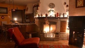 Un salon chaleureux avec une cheminée, un fauteuil rouge et un coin repas comprenant une table et des chaises.