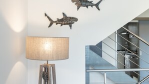 Un interior moderno con una escalera, una lámpara de pared y dos obras de arte con forma de tiburón.