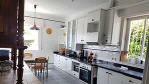 A modern kitchen with white cabinets, a black countertop, and a built-in oven. There is a dining table with chairs and a window with greenery outside. - House on the Mediterranean, swimming pool, BBQ Garden, WiFi, air conditioning (Rincon de la Victoria)