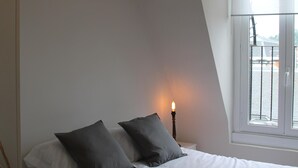 A bedroom with a bed, a hanging lamp, a bedside table with a candle, and a window with a view. - Apartment overlooking the cathedral, terrace, wifi, parking included (Donostia)