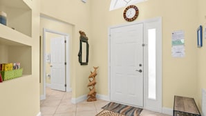 A hallway with a white door, a clock, a patterned rug, and a shelf with books.