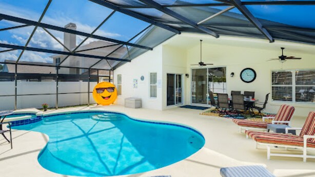 A covered outdoor swimming pool with lounge chairs and a ceiling fan.