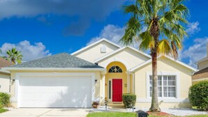 A single-story house with a white garage, a red door, and a palm tree in the front yard.