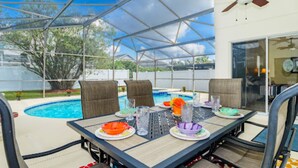 An outdoor patio with a pool, a table set for dining, and chairs.