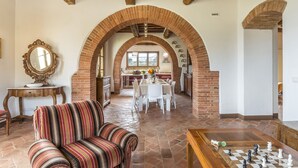 A spacious living area with a striped sofa, a chess table, and a dining area with a brick archway. - Bossoncina 8+1, Emma Villas (Montepulciano)