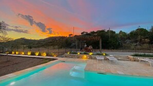 Piscina con vista al atardecer, asientos exteriores y una zona cubierta con gente.