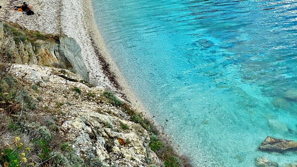 Un paisaje costero con un mar turquesa transparente, acantilados rocosos y vegetación escasa.