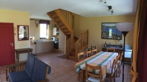 A spacious kitchen with wooden cabinets, a dining area with a table and chairs, a staircase, and a painting on the wall.