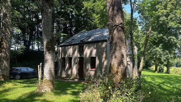 A small, single-story building surrounded by trees, with a car parked in front.