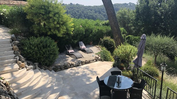 A patio with a round table and chairs, surrounded by a stone wall and various plants. - CHARMING VILLA 💖Panoramic views of sea & mountain, private sunny terraces, pool (Saint-Paul-De-Vence)